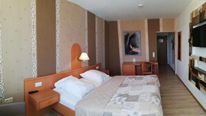 Une chambre d’hôtel équipée d’un lit, d’une table de chevet, d’une lampe, d’un bureau, d’une chaise et d’un téléviseur fixé au mur.