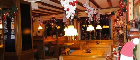 A restaurant interior with wooden tables and benches, festive decorations, and warm lighting.