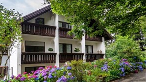 Un bâtiment à deux étages doté de balcons, entouré d’une végétation luxuriante et de fleurs aux couleurs vives.