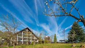 Un hôtel à la façade traditionnelle en bois, doté d’une grande pelouse et surplombant un ciel d’un bleu éclatant.