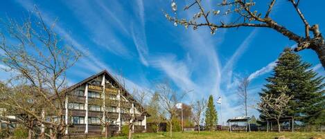 A hotel with a traditional wooden facade, a large open lawn, and a clear blue sky.