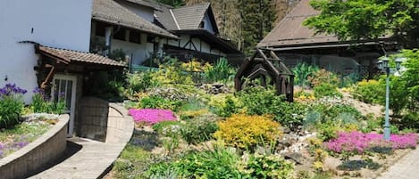A traditional European-style building with a stone pathway leading to a garden with colorful flowers and plants.