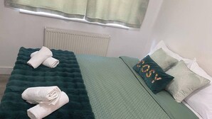 En snyggt bäddad säng med ett grönt täcke, två kuddar och två hopvikta handdukar.