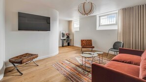 A modern living room with a flat-screen TV, a tufted ottoman, a patterned rug, and a red sofa. - Spacious Apartment  a/c 1BR/4P - Notre-Dame (Paris)