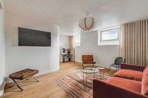 A modern living room with a flat-screen TV, a tufted ottoman, a patterned rug, and a red sofa. - Spacious Apartment  a/c 1BR/4P - Notre-Dame (Paris)