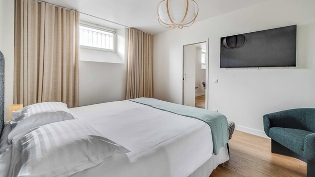 A hotel room with a bed, curtains, a chair, a TV, and a door. - Spacious Apartment  a/c 1BR/4P - Notre-Dame (Paris)