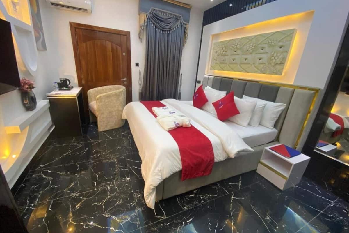 A modern hotel room with a large bed, a desk, a chair, and a vanity with a mirror.