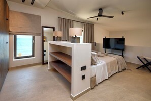 Habitación de hotel moderna con una cama grande, televisión, ventilador de techo y ventana con vista al mar.