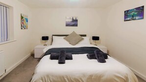A neatly made bed with pillows and rolled towels, a bedside table with a lamp, and a painting on the wall. - Step-Free Bungalow w/ Garden & Parking, Near LGW (Wallington, Surrey)