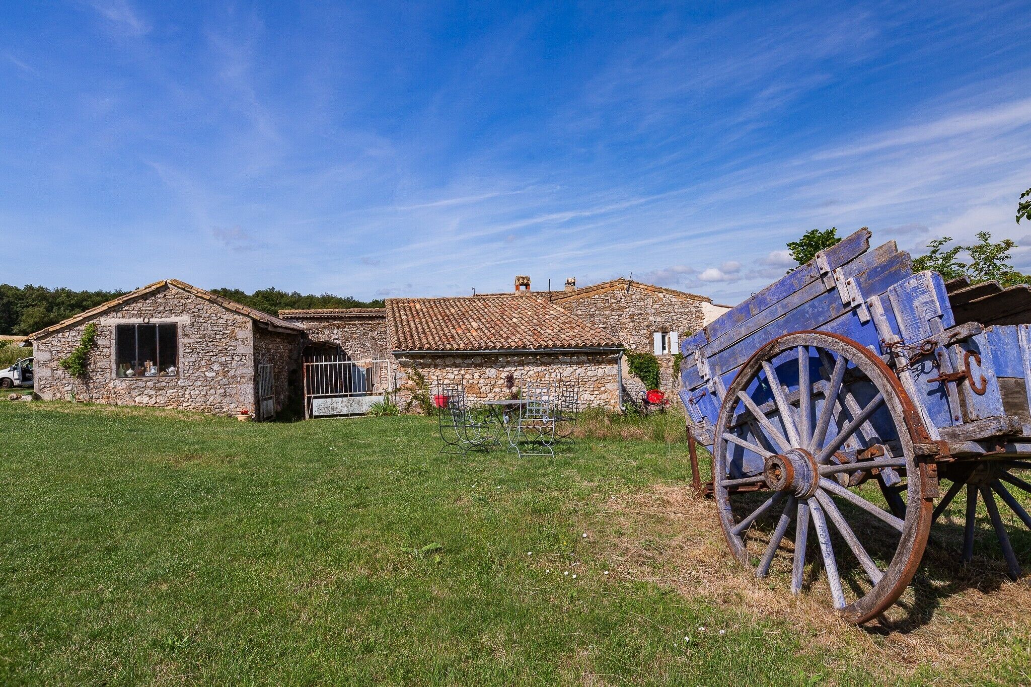 Ein rustikales Steinhaus mit Ziegeldach, einem Metallgitter und einem großen Holzwagen.