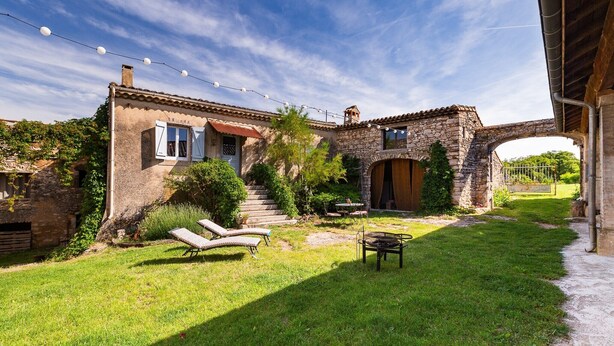 Una casa de piedra con jardín, mobiliario exterior y un arco de piedra.