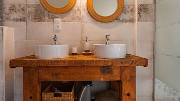 Ein Badezimmer mit zwei Waschbecken, einem Holzkosmetikschrank, zwei runden Spiegeln und einer gefliesten Wand.