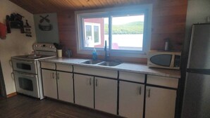 Una cocina con techo de madera, ventana con vista a un lago, estufa, fregadero y refrigerador.