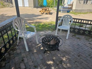 Un'area patio con due sedie bianche, un braciere in metallo e un tavolo in legno.
