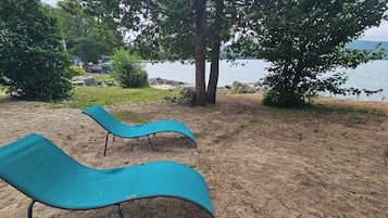 Deux fauteuils bleus sont placés sur une plage de sable, offrant une vue sur l’eau et les arbres qui se dressent à l’arrière-plan.