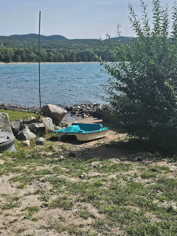 A boat on a sandy shore near a body of water with a forested hill in the background.