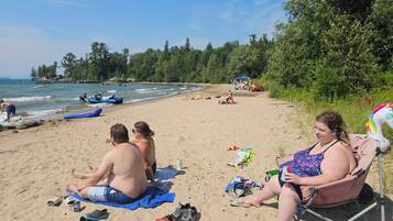 A beach scene with people relaxing on towels and chairs, a tent, and a unicorn floatie.