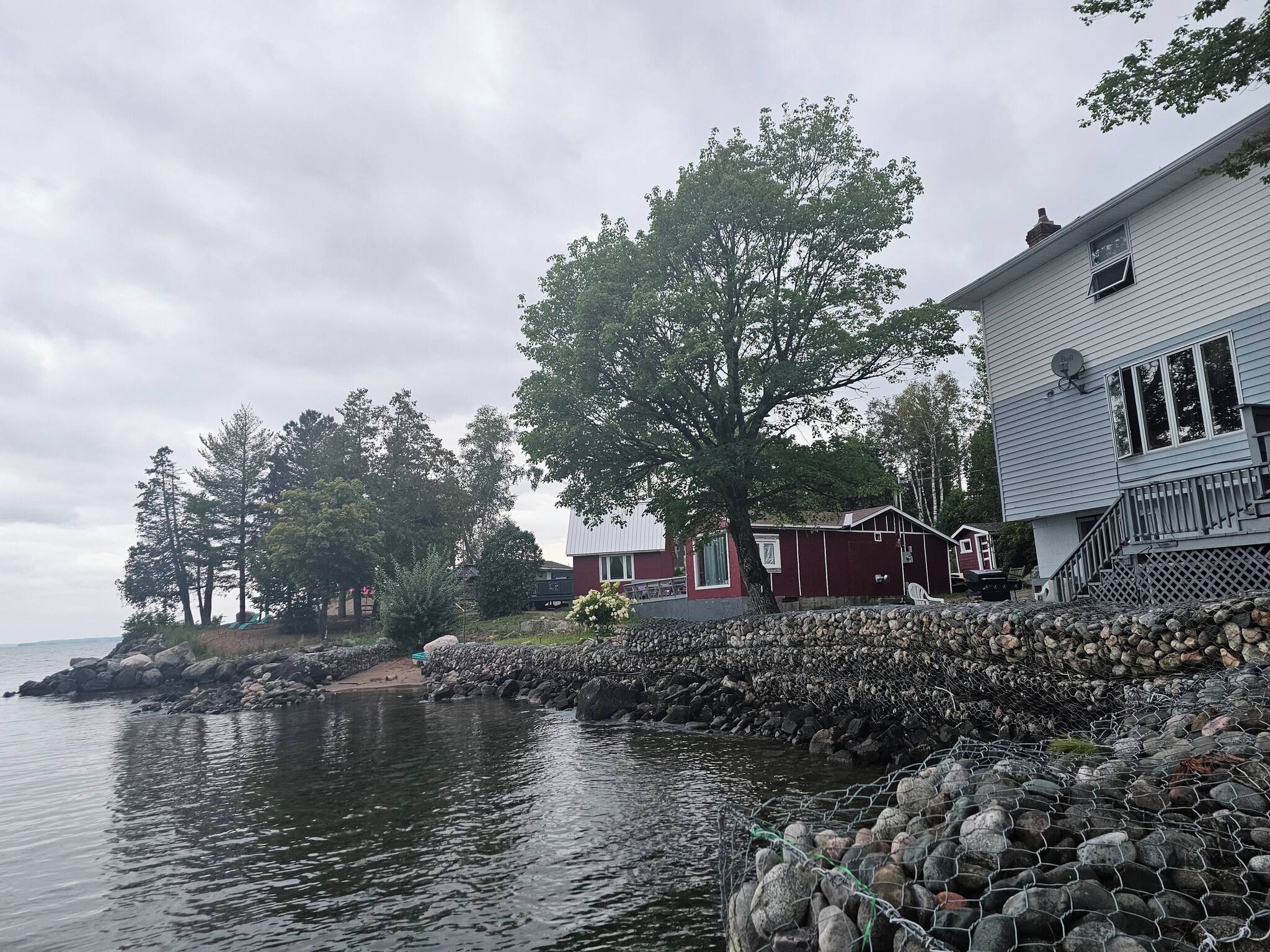 Une propriété située au bord de l’eau, avec une maison adjacente à une côte rocheuse, un mur de pierres et une étendue d’eau calme.