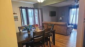 Un comedor con una mesa y sillas de madera, un jarrón de flores y una ventana con cortinas.