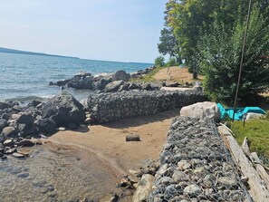 A rocky shoreline with clear water, a stone wall, and a green chair.