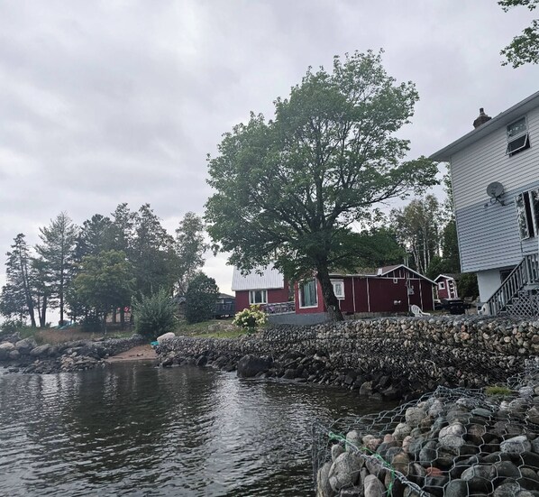 A waterfront property with a stone wall, a large tree, and a red house. - Lake Superior Waterffront Main Unit of Duplex Sleeps 8 ppl (Unorganized North Algoma)