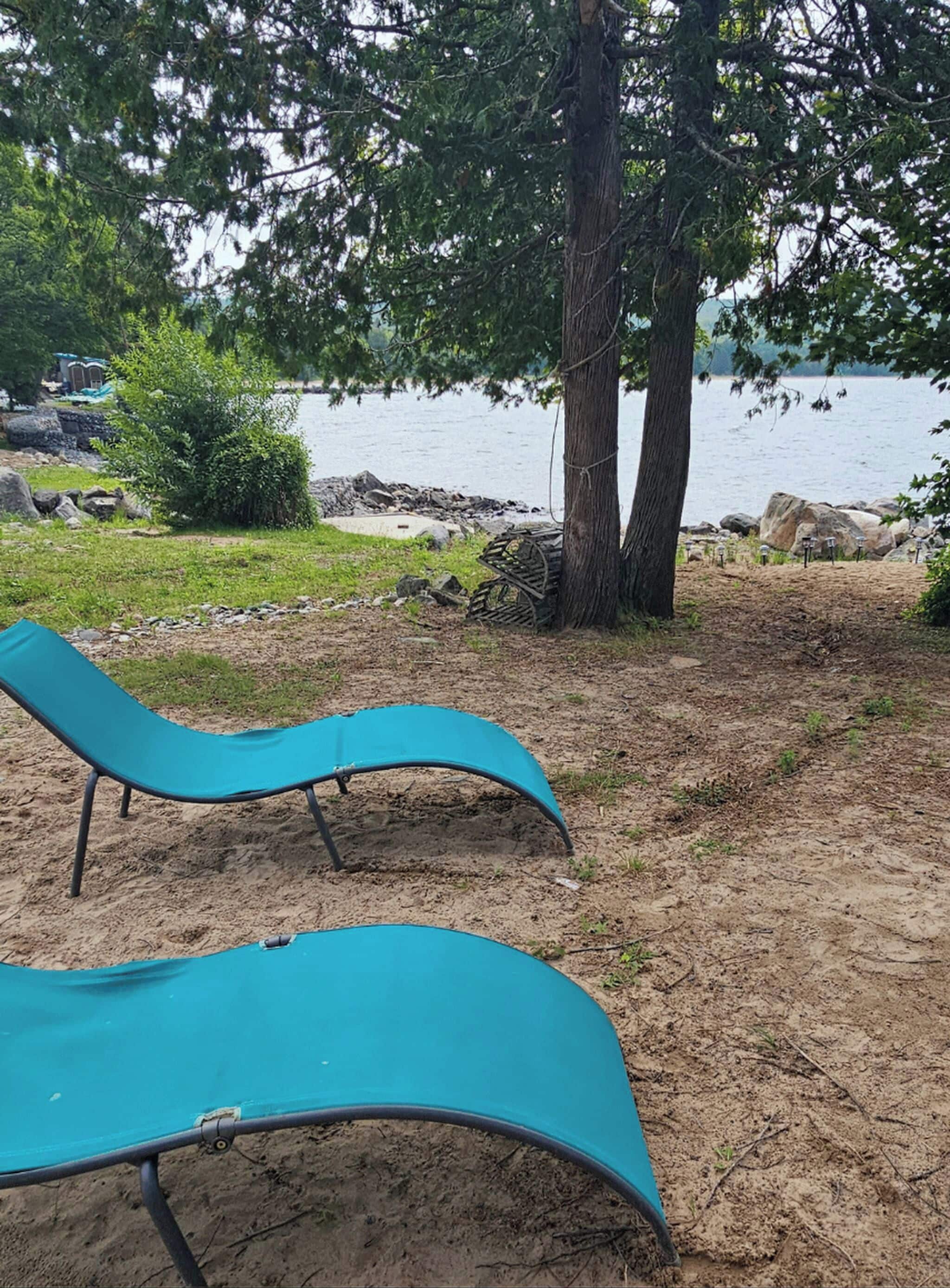 Dos sillones azules cerca de un lago, con un árbol y rocas al fondo.