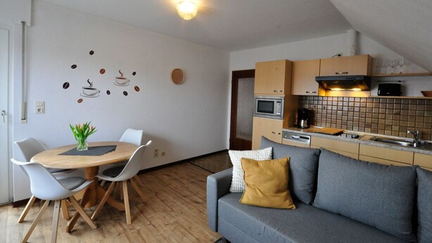 Una cocina compacta con microondas, cafetera y un pequeño comedor con mesa y sillas.
