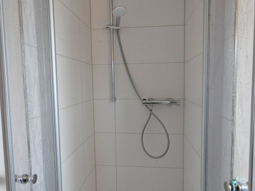 Een douche met een handdouche en een vastzitende kraan aan de muur.