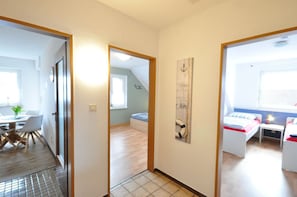 A narrow hallway leading to a dining area with a table and chairs, a bedroom with a bed and bedside table, and a small window with a view. - Haus Pithan - House Pithan in Werdum - Holiday home with garden, WLAN and 4 (Werdum)