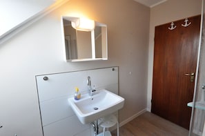 A bathroom with a white sink, a mirror, and a wooden door. - Haus Pithan - House Pithan in Werdum - Holiday home with garden, WLAN and 4 (Werdum)