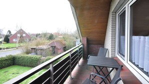 Un balcón con una mesa y sillas, con vista a una zona residencial con casas y una calle.