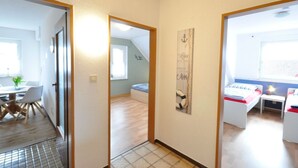 Un pasillo estrecho que conduce a un comedor con mesa y sillas, un dormitorio con cama y mesita de noche, y un ventanal con vistas.