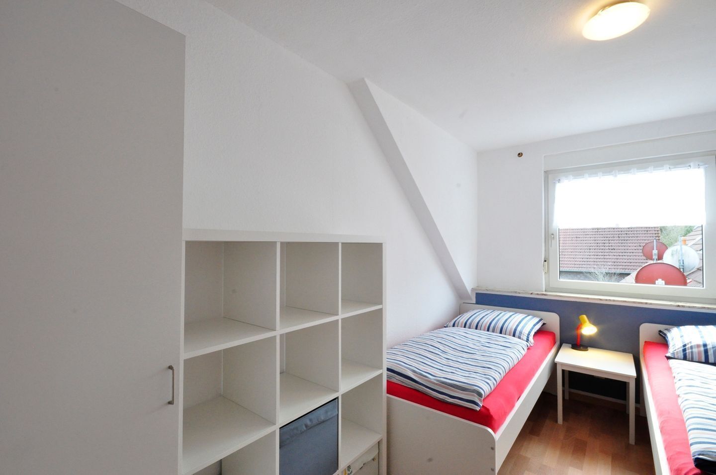 Un dormitorio con dos camas, una ventana y estanterías empotradas.