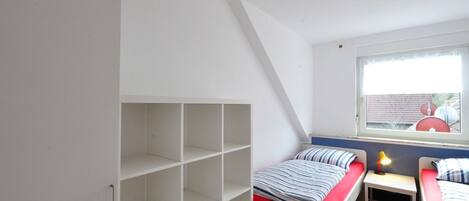 Un dormitorio con dos camas, una ventana y estanterías empotradas.