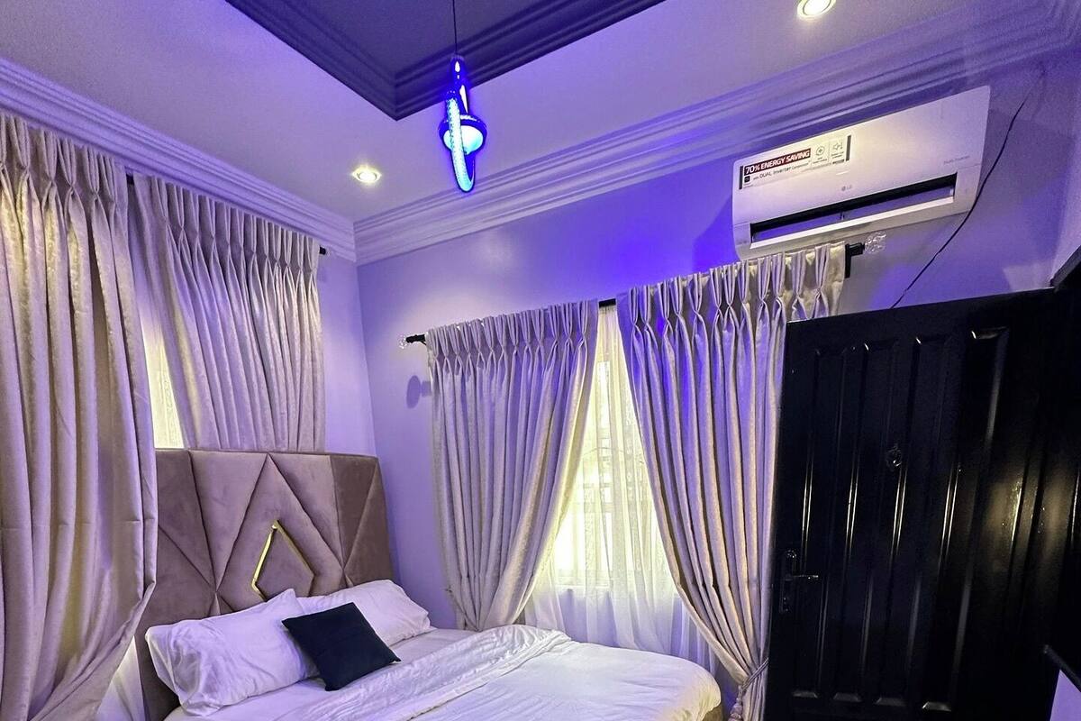 A modern bedroom with a large bed, a nightstand, an air conditioning unit, and a wardrobe.