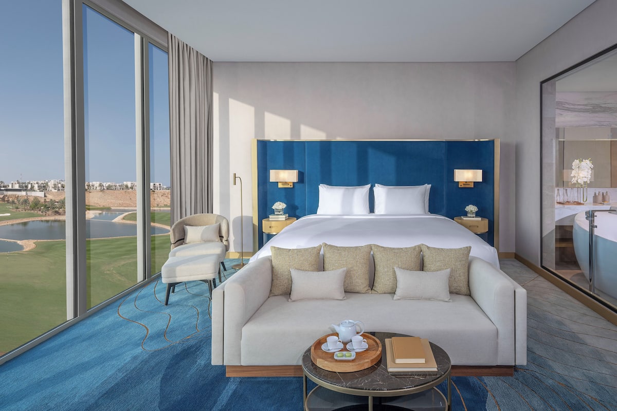 Une chambre d’hôtel moderne dotée d’un grand lit, d’un canapé, d’une table à manger et offrant une vue sur un terrain de golf.