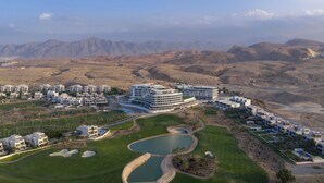 Um hotel moderno com vários edifícios, um campo de golfe e uma paisagem desértica ao fundo.