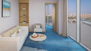 A modern hotel room with a sofa, a small table with a teapot, a bookshelf, and a balcony with a view. - Tivoli LA VIE Muscat Hotel & Residences (Muscat)