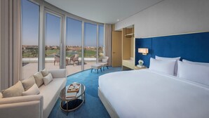 Habitación de hotel con una cama grande, un sofá, una mesita con bandeja, una silla y vistas a un campo de golf.