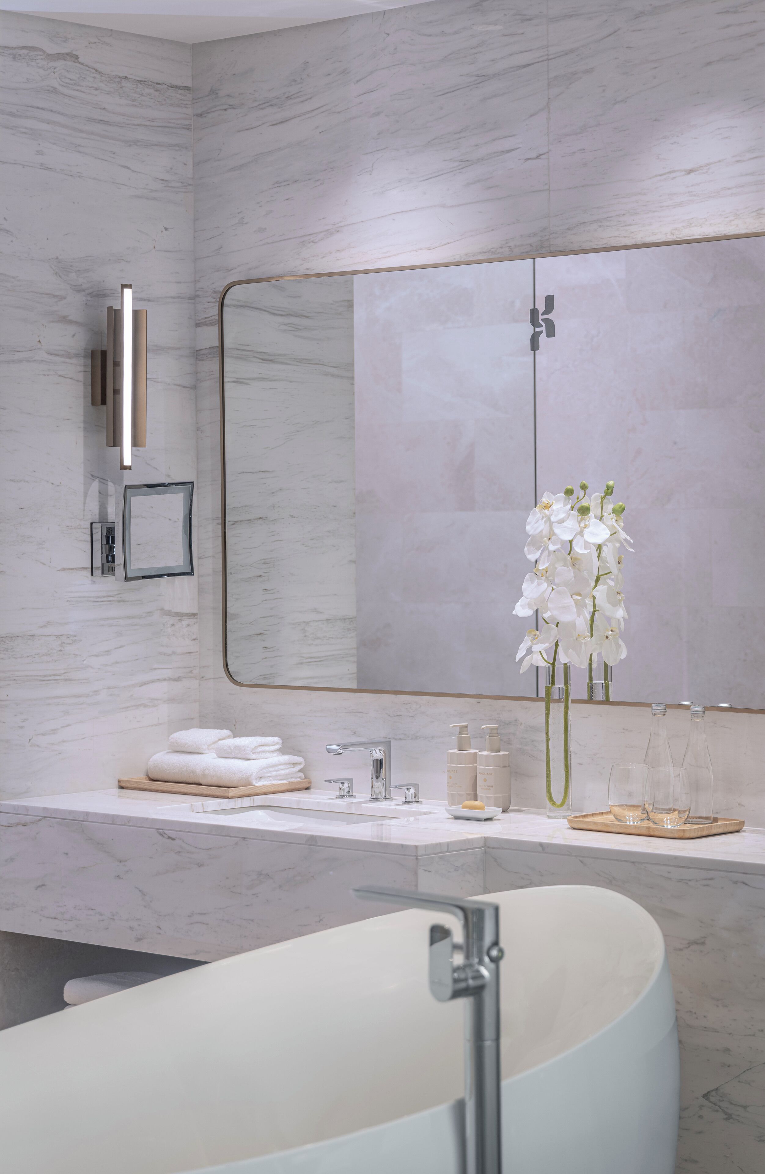 A modern bathroom with a freestanding bathtub, a large mirror, and a vase with white flowers.