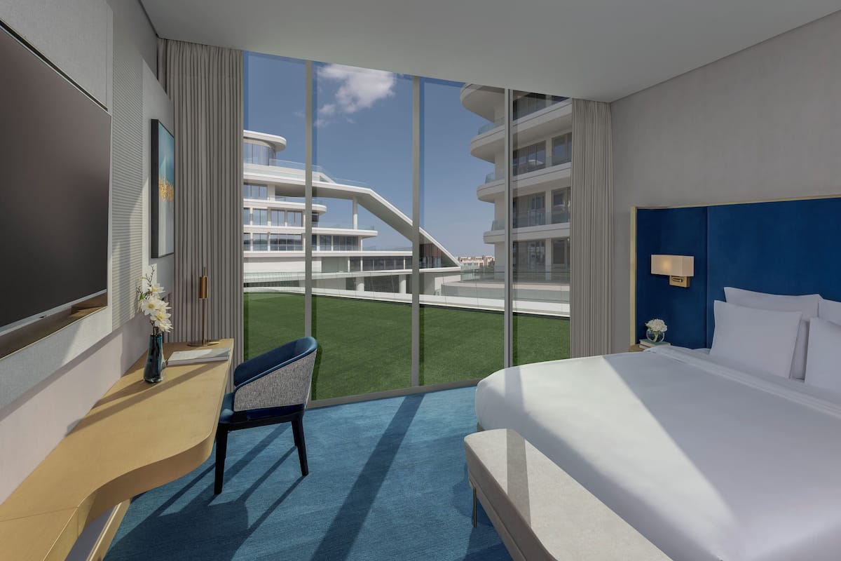 Une chambre d’hôtel moderne, dotée d’un grand lit, d’un bureau, d’une chaise et offrant une vue sur un immeuble grâce à de grandes fenêtres.