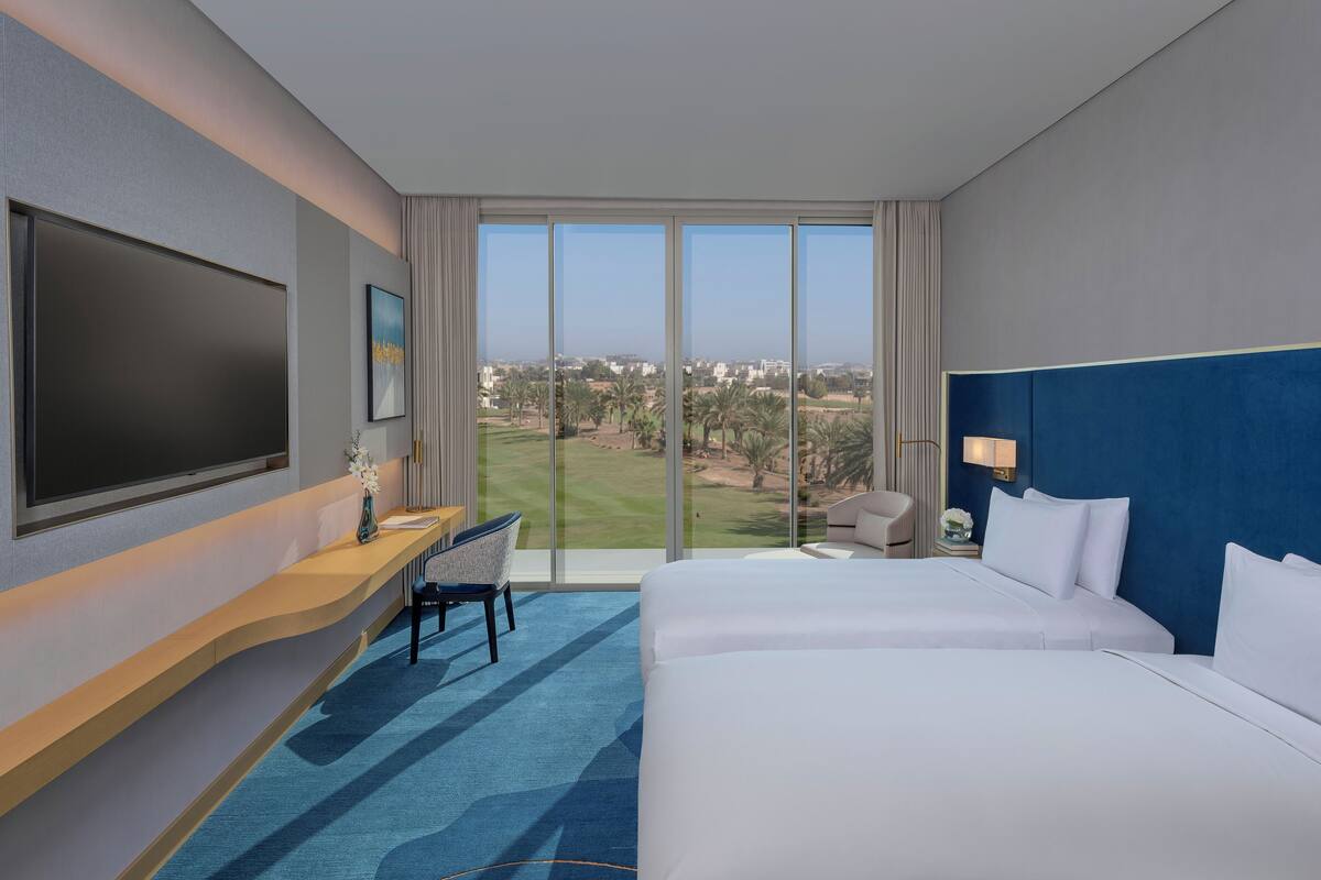 Une chambre d’hôtel avec un grand lit, un bureau avec une chaise, une télévision et une vue sur un terrain de golf.