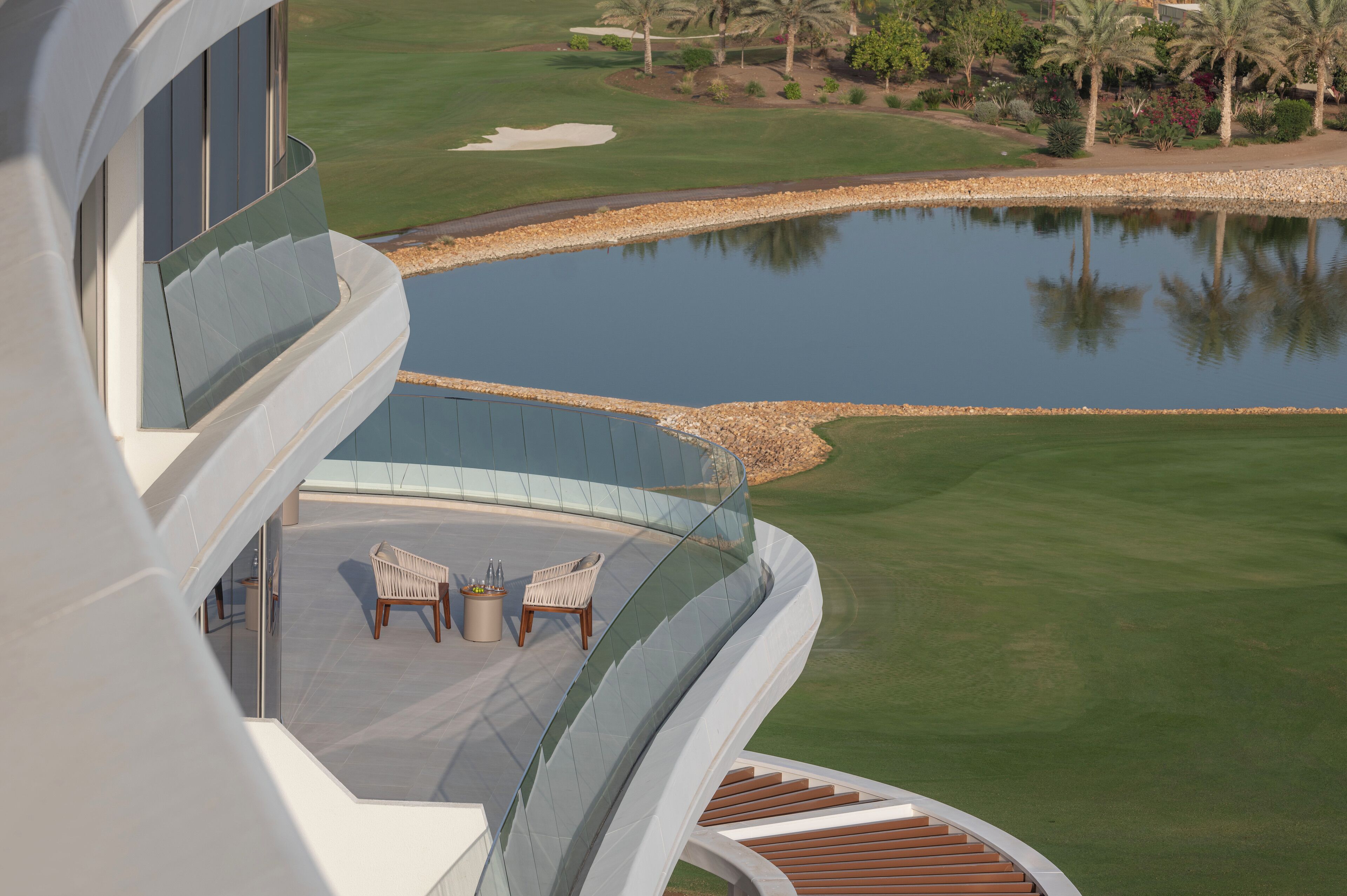 A modern building with a pool, a golf course, and two chairs on a balcony.