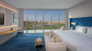 A hotel room with a large window, a bed, a desk, a chair, and a small table with a tray. - Tivoli LA VIE Muscat Hotel & Residences (Muscat)