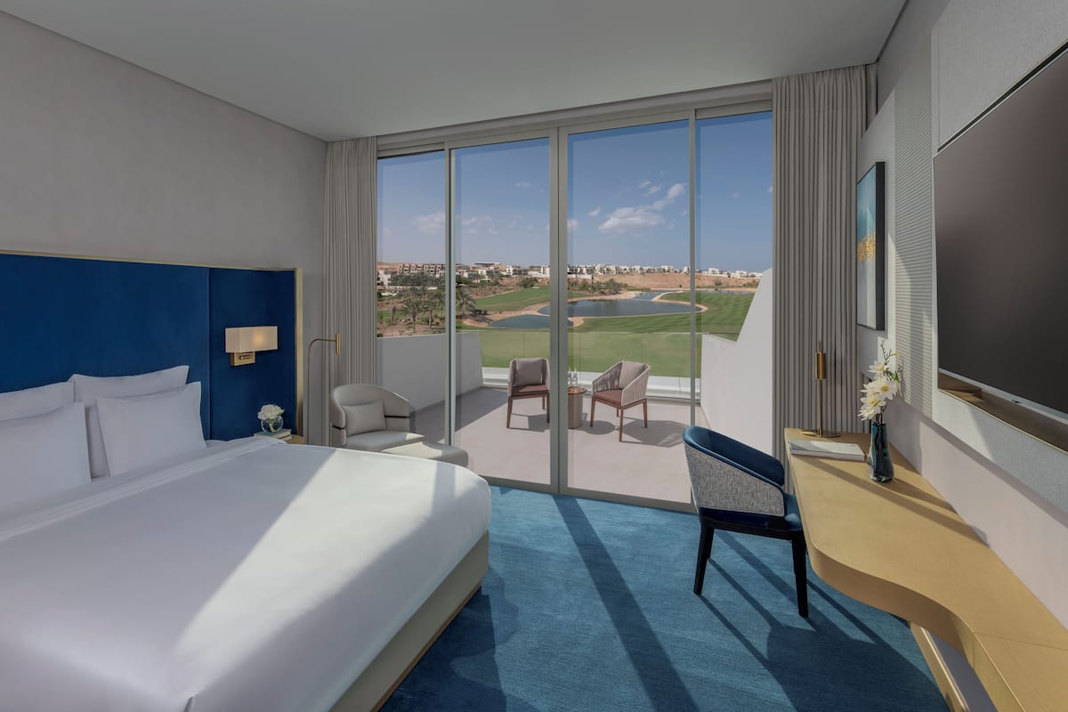 Une chambre d’hôtel avec un grand lit, un bureau, une chaise et une vue sur un terrain de golf.
