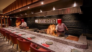 A restaurant with a long counter, red chairs, and chefs cooking with flames. - Tivoli LA VIE Muscat Hotel & Residences (Muscat)