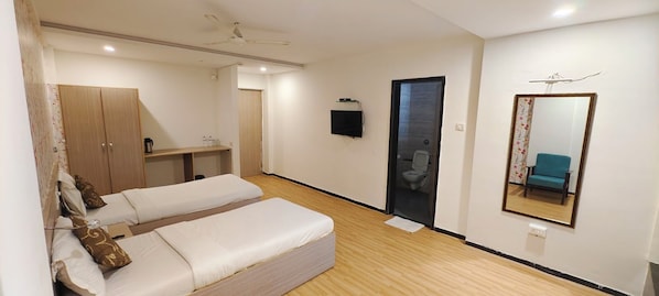 A room with two beds, a wardrobe, a TV, a mirror, and a bathroom door. - HOTEL OASIS SURAT PVT. LTD. (Surat)