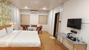 Ett hotellrum med en stor säng, två stolar, ett litet bord, en TV och en minibar.