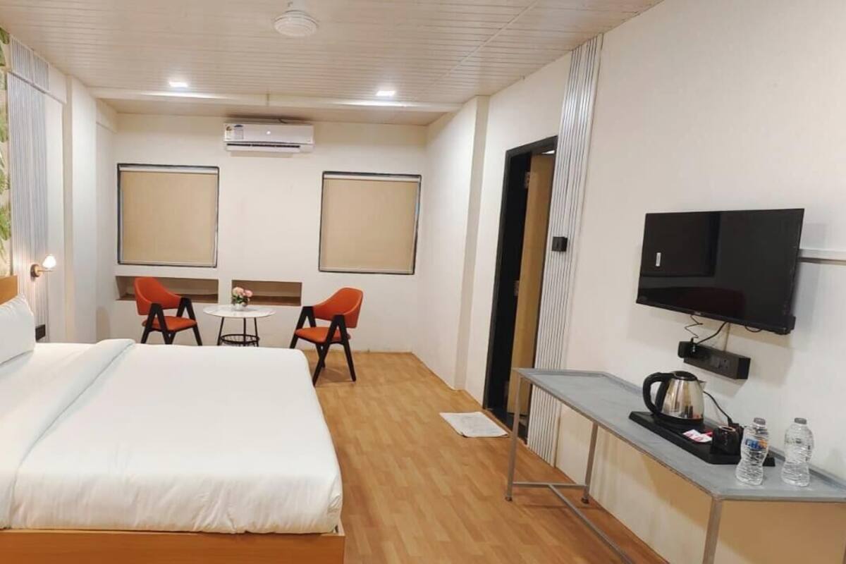A hotel room with a large bed, two chairs, a small table, a TV, and a minibar.