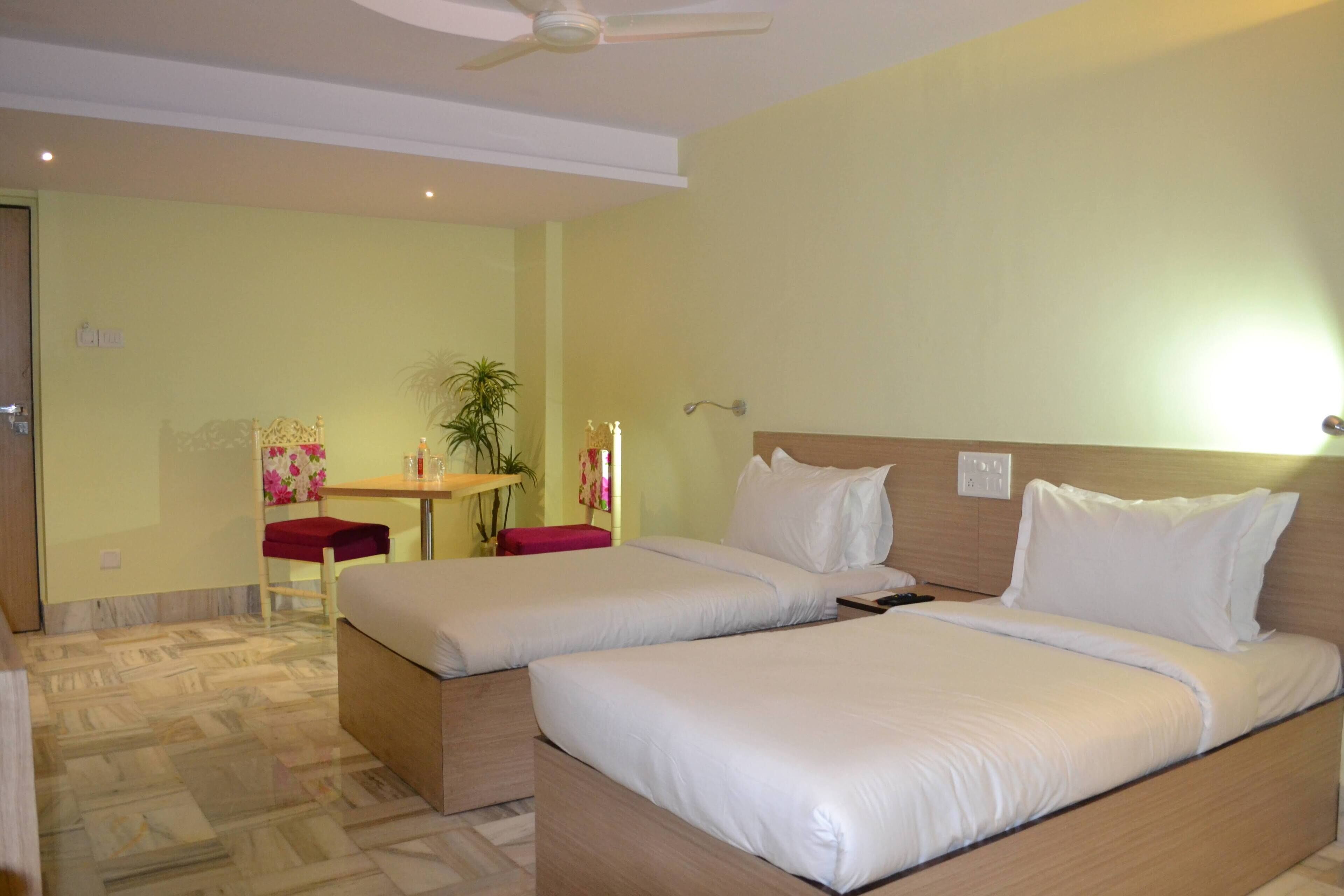 A hotel room with two beds, a desk, a chair, and a plant.
